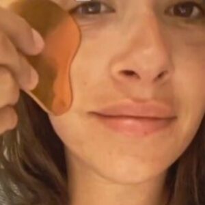 Persona realizando un masaje facial con una Gua Sha de cobre sobre la mejilla.